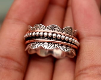 May include: A silver and copper spinner ring with a textured design. The ring has a wavy edge and a row of beads.