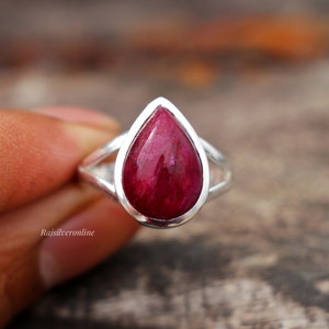 Può includere: Un anello con rubino a forma di lacrima incastonato in argento sterling. L'anello ha un design delicato e traforato e una pietra preziosa di colore rosso intenso.