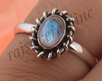 May include: A silver ring featuring an oval-shaped moonstone cabochon set in a decorative, twisted rope-style bezel. The band is smooth and polished, while the setting has a darkened, oxidised finish to highlight the intricate metalwork details.