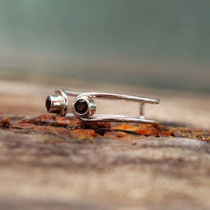 May include: A silver ring with two red gemstones set in the band. The ring is designed with two parallel bands that are connected by a small loop.
