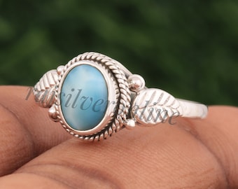 May include: A sterling silver ring featuring an oval-shaped, light blue Larimar gemstone set in a twisted rope border. The band is decorated with detailed leaf motifs on both sides of the central stone setting, creating a nature-inspired design.