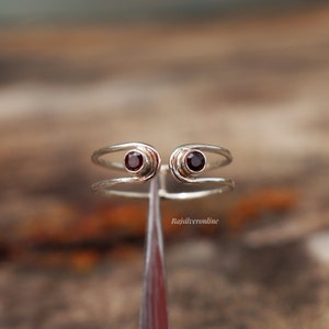 May include: A silver ring with two red gemstones set in the band. The ring is designed to be worn on the knuckle.