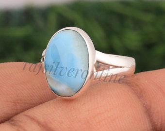 May include: A silver ring featuring a large, smooth, oval-shaped light blue stone with white marbled patterns. The stone is set in a polished silver bezel, and the band is made of a simple, solid silver metal that splits into two thin arms.