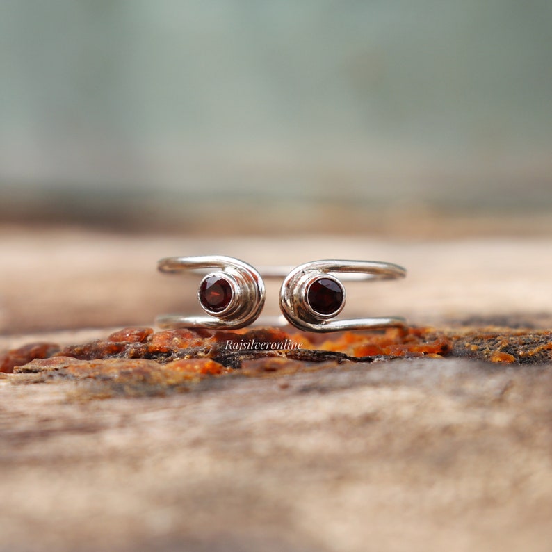 May include: A silver ring with two red gemstones set in the band. The ring is designed to be worn on the knuckle of a finger.