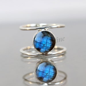 May include: A silver ring featuring a blue labradorite gemstone set in a double band design.