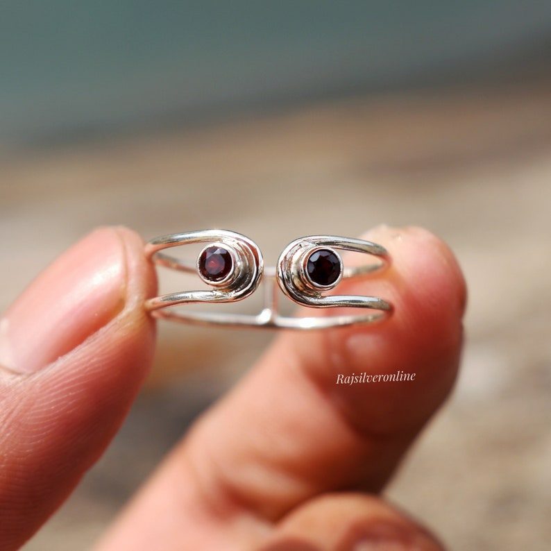 May include: A silver ring with two red gemstones set in the band. The ring is open and adjustable.