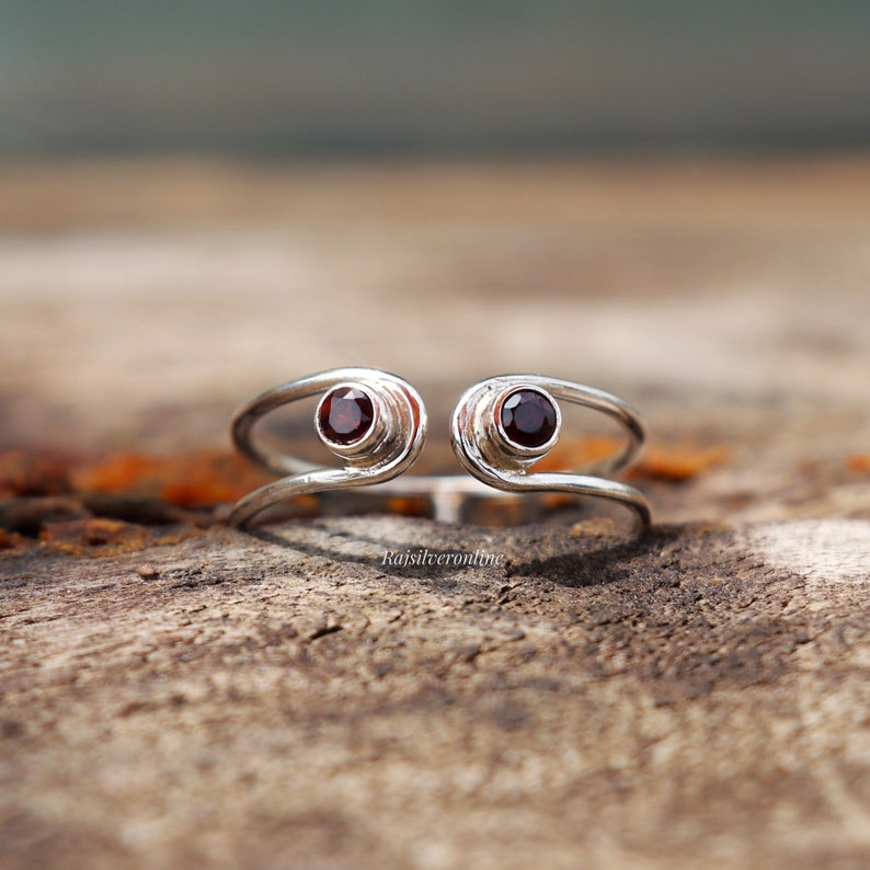 May include: A silver ring with two red gemstones set in the band. The ring is designed to be worn on the finger.