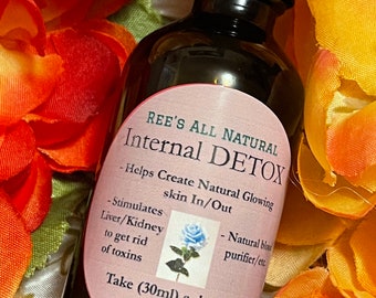 May include: A dark brown glass bottle with a black cap, labeled "REE'S ALL NATURAL Internal DETOX." The label includes text about skin health and detoxification, with a blue rose illustration. The bottle is surrounded by orange and yellow flowers.