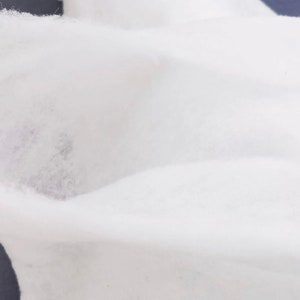 K&ouml;nnte beinhalten: Wei&szlig;er Baumwollstoff mit einer weichen, strukturierten Oberfl&auml;che. Der Stoff ist gefaltet und drapiert, wodurch seine Textur und sein Fall sichtbar werden.