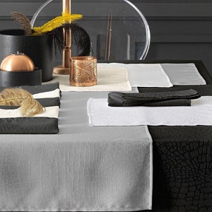 May include: A black table setting with a gray and white striped placemat, a black placemat, and a white placemat. There are also two black napkins and a copper candle holder.