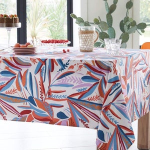 May include: A white tablecloth with a colorful abstract pattern of leaves and branches in shades of red, orange, blue, and purple. The tablecloth is laid on a wooden table with a pitcher and glasses on top.