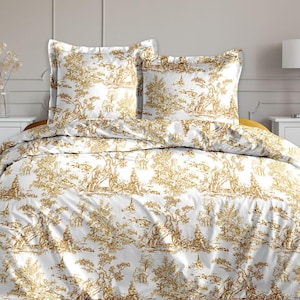 Peut inclure: Une parure de lit blanche et dorée avec un motif de toile de Jouy détaillé. L'ensemble comprend une housse de couette et deux taies d'oreiller. La literie est posée sur un lit avec un accent jaune. La pièce a une palette de couleurs neutres.