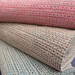 Peut inclure: Gros plan sur trois rouleaux de tissu texturé. Le rouleau supérieur est rouge foncé avec un motif carré tissé. Le rouleau du milieu est beige neutre avec des accents noirs et bruns. Le rouleau inférieur est bleu-vert avec un motif similaire.