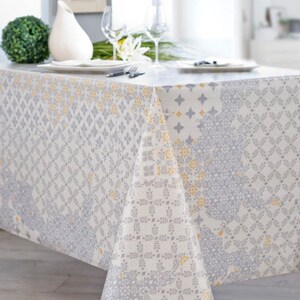May include: A white tablecloth with a gray and yellow geometric pattern. The tablecloth is laid out on a table with a vase and flowers on top.