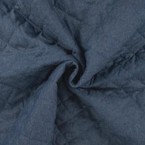 Può includere: Primo piano di un tessuto trapuntato in un blu indaco intenso. Il tessuto presenta un motivo a rombi creato da linee cucite. Il materiale è morbido e appare leggermente stropicciato, con pieghe e curve che aggiungono consistenza.