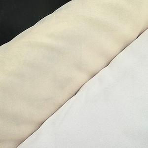 Peut inclure: Trois rouleaux de tissu disposés en diagonale, comprenant un textile noir uni en haut, un textile beige uni au centre et un textile blanc uni en bas. Chaque rouleau présente une texture finement tissée et uniforme sur toute la surface.