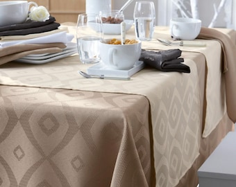 Puede incluir: Un mantel de mesa estampado en beige y marrón con un diseño geométrico. El mantel está puesto con un cuenco de cerámica blanca, un vaso de agua y una taza de cerámica blanca. También hay servilletas negras y un plato blanco en la mesa.
