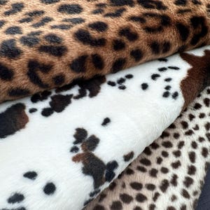 Puede incluir: Primer plano de tres telas de piel sintética. La tela superior tiene un estampado de leopardo marrón y negro. La tela del medio es blanca con manchas de vaca marrones y negras. La tela inferior tiene un estampado de guepardo marrón y beige.