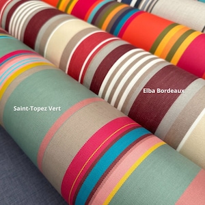 Pode incluir: V&aacute;rios rolos de tecido &agrave;s riscas com v&aacute;rias combina&ccedil;&otilde;es de cores. Um rolo est&aacute; etiquetado como Saint-Topez Vert com riscas verde-s&aacute;lvia, rosa, amarelo e turquesa. Outro rolo est&aacute; etiquetado como Elba Bordeaux com riscas bordeaux, branco e bege.