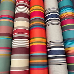 Könnte beinhalten: Fünf Rollen gestreiften Stoffes in verschiedenen Farben, darunter Türkis, Rot, Orange, Beige und Marineblau. Der Stoff hat ein horizontales Streifenmuster.