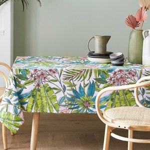 Peut inclure: Une nappe blanche avec un imprimé de feuilles et de fleurs tropicales. La nappe est posée sur une table avec deux chaises. Il y a des plats et un pichet sur la table.