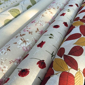 Peut inclure: Plusieurs rouleaux de tissu avec des motifs floraux et de feuilles. Les tissus pr&eacute;sentent des motifs de fleurs blanches et roses, de coquelicots rouges et divers motifs de feuilles en vert, jaune et rouge. Les rouleaux de tissu sont beiges et cr&egrave;me.