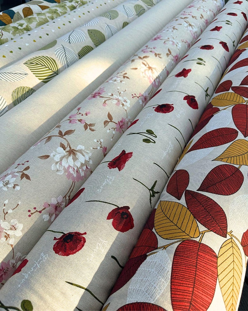 Peut inclure: Plusieurs rouleaux de tissu avec des motifs floraux et de feuilles. Les tissus pr&eacute;sentent des motifs de fleurs blanches et roses, de coquelicots rouges et divers motifs de feuilles en vert, jaune et rouge. Les rouleaux de tissu sont beiges et cr&egrave;me.