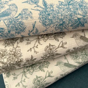 Peut inclure: Gros plan sur trois tissus pliés avec des motifs floraux et d'oiseaux. Le tissu supérieur présente des oiseaux et des fleurs bleus sur un fond crème. Le tissu du milieu a des motifs floraux bruns et le tissu inférieur a des motifs floraux verts.