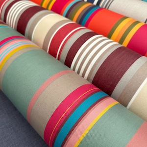 Pode incluir: V&aacute;rios rolos de tecido dispostos lado a lado, cada um apresentando padr&otilde;es distintos de listras verticais. As cores incluem tons vibrantes de laranja, rosa choque, turquesa, amarelo, bord&ocirc;, verde s&aacute;lvia, bege e branco.