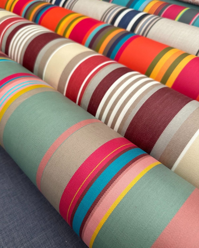 Pode incluir: V&aacute;rios rolos de tecido dispostos lado a lado, cada um apresentando padr&otilde;es distintos de listras verticais. As cores incluem tons vibrantes de laranja, rosa choque, turquesa, amarelo, bord&ocirc;, verde s&aacute;lvia, bege e branco.
