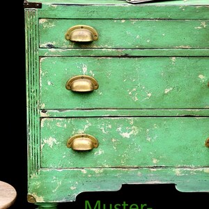 K&ouml;nnte beinhalten: Eine gr&uuml;n lackierte Kommode aus Holz mit vier Schubladen und Messinggriffen. Die Kommode hat eine abgenutzte Oberfl&auml;che und steht auf einem schwarzen Hintergrund. Der Text "Muster-Beispiel" ist in Gr&uuml;n unter der Kommode geschrieben.