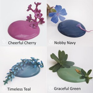 K&ouml;nnte beinhalten: Vier Farbmuster mit Blumenakzenten. Die Farben sind Cheerful Cherry, ein kr&auml;ftiges Pink, Timeless Teal, ein Blaugr&uuml;n, Nobby Navy, ein Dunkelblau, und Graceful Green, ein gedecktes Gr&uuml;n.