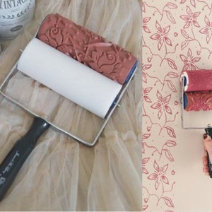 Könnte beinhalten: Eine doppelseitige Farbrolle mit einem Blumenmuster. Die Rolle wird verwendet, um einen Muster-Effekt auf einer Wand zu erzeugen. Die Rolle wird in zwei Bildern gezeigt, einmal auf einer weißen Oberfläche und einmal beim Einsatz an einer Wand.