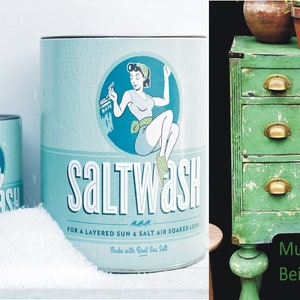 Könnte beinhalten: Zwei blaue und weiße Dosen mit Saltwash-Farbe mit einer Vintage-Illustration einer Frau, die malt. Der Text auf den Dosen lautet "Saltwash" und "Für einen geschichteten Sonnen- und Salzwasser-Look. Hergestellt mit echtem Meersalz."