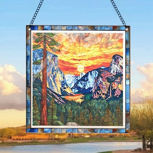 May include: A stained glass window hanging with a depiction of a mountain range with a lake and a sunset. The mountains are blue and purple, the lake is blue, and the sunset is orange and yellow. There are trees in the foreground.