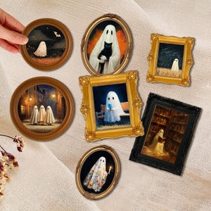 May include: A collection of framed art pieces featuring whimsical ghost illustrations. The frames vary in shape and color, including round, oval, and rectangular designs. The artwork depicts ghosts in various settings, such as a library, holding a cat, and in a field.