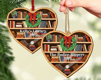 May include: Heart-shaped wooden ornament featuring a bookshelf design filled with books. A red bow and green wreath are centered. The text "Kelly's Library 2025" and "The Bodice Rippers 2025" are displayed. A red ribbon and twine are attached.