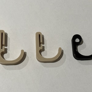 May include: Three plastic hooks, two are beige and one is black. The hooks are designed to hang items on a wall or other surface.