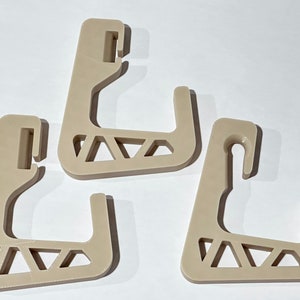 May include: Three beige plastic hooks with a geometric design. The hooks are designed to hang items on a wall or other surface.