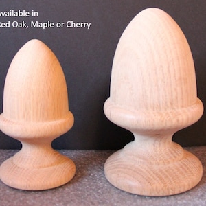 May include: Two wooden finials in the shape of acorns. The finials are available in red oak, maple, or cherry. The larger finial is on the right and the smaller finial is on the left.