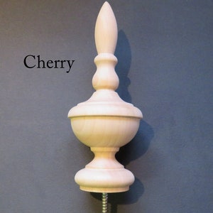 May include: A wooden finial with a cherry wood finish. The finial has a bulbous base and a pointed top. It is designed to be attached to furniture or other objects.