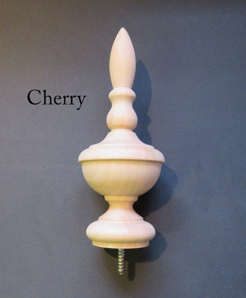 May include: A wooden finial with a cherry wood finish. The finial has a bulbous base and a pointed top. It is designed to be attached to furniture or other objects.
