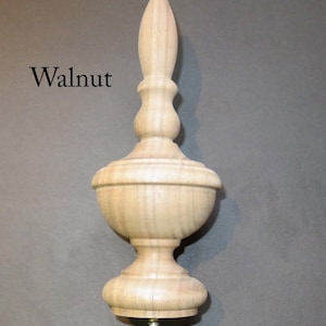 May include: A wooden finial in walnut with a pointed top and a screw base. The finial is a decorative element used on furniture, cabinets, and other objects.