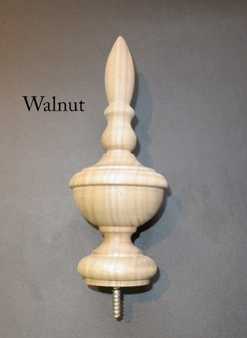 May include: A wooden finial in walnut with a pointed top and a screw base. The finial is a decorative element used on furniture, cabinets, and other objects.