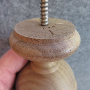 May include: Close-up of a wooden finial with a threaded metal rod inserted through the top. The finial has a rounded top and a smooth, light brown finish.