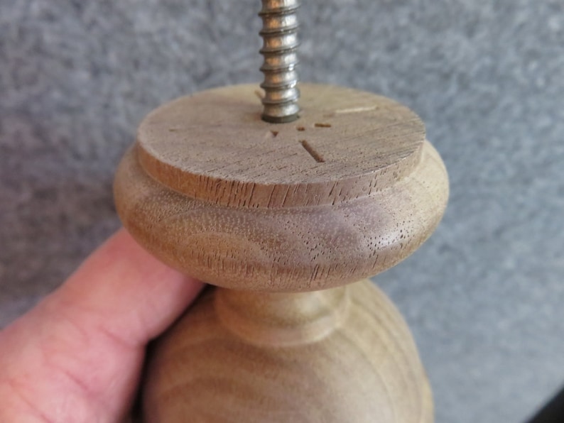 May include: Close-up of a wooden finial with a threaded metal rod inserted through the top. The finial has a rounded top and a smooth, light brown finish.