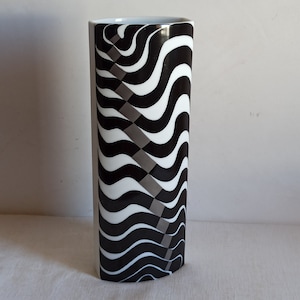 May include: Tall, cylindrical vase with a black and white wavy pattern. The design features alternating black and white curved lines, with a section of gray and white checkered pattern. The vase has a white interior.