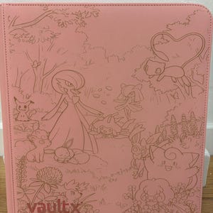 May include: A light pink binder featuring a detailed line art illustration of various Pokémon characters in a forest setting. The front cover displays the Vault X logo in the bottom left corner, with a textured surface and stitched edges.