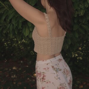 May include: A woman wearing a beige crochet top and a white floral skirt. The top is a cropped style and the skirt is a flowy, wide-leg style.