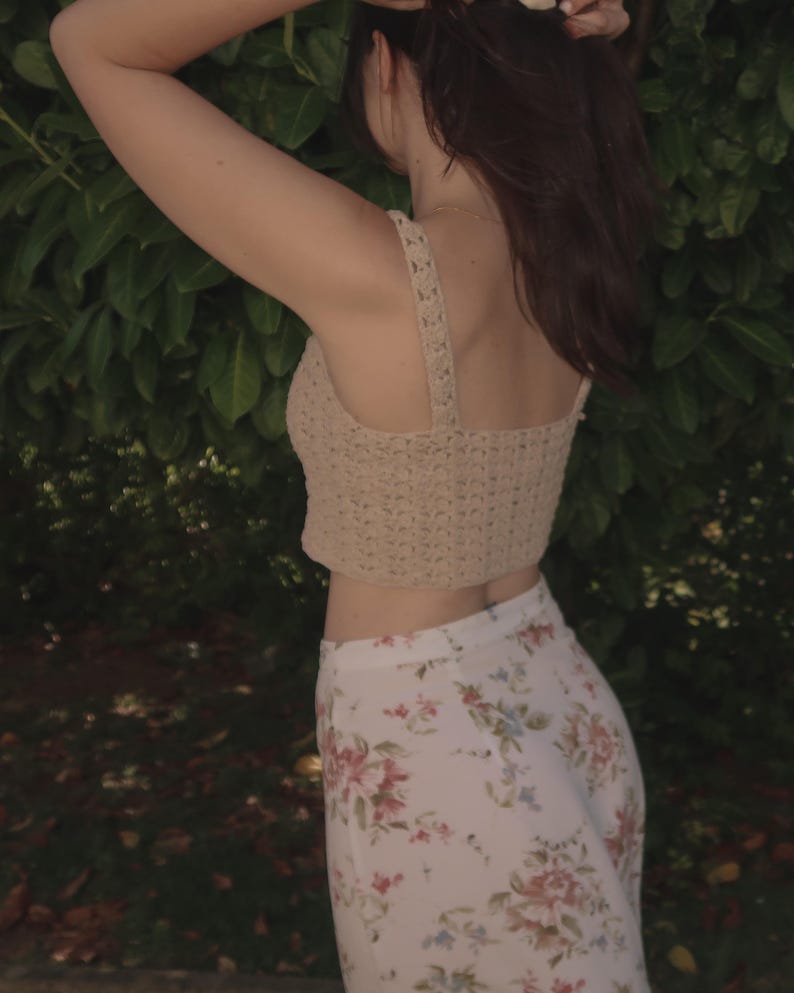 May include: A woman wearing a beige crochet top and a white floral skirt. The top is a cropped style and the skirt is a flowy, wide-leg style.